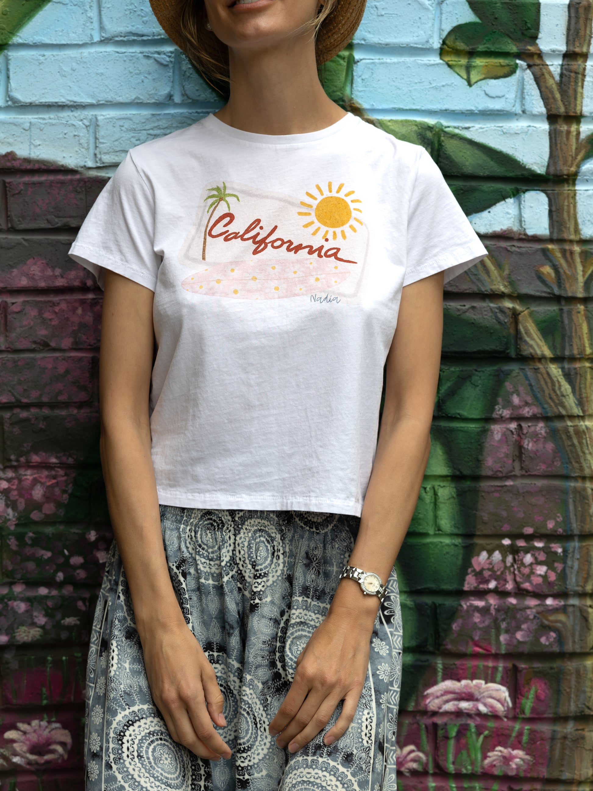 This tee is a Golden State of mind come true, featuring a hand-drawn design that's as cool as a Pacific Ocean breeze. A California license plate gets a rad makeover with a pink floral surfboard, palm tree, and sun - it's like a vacation for your wardrobe!