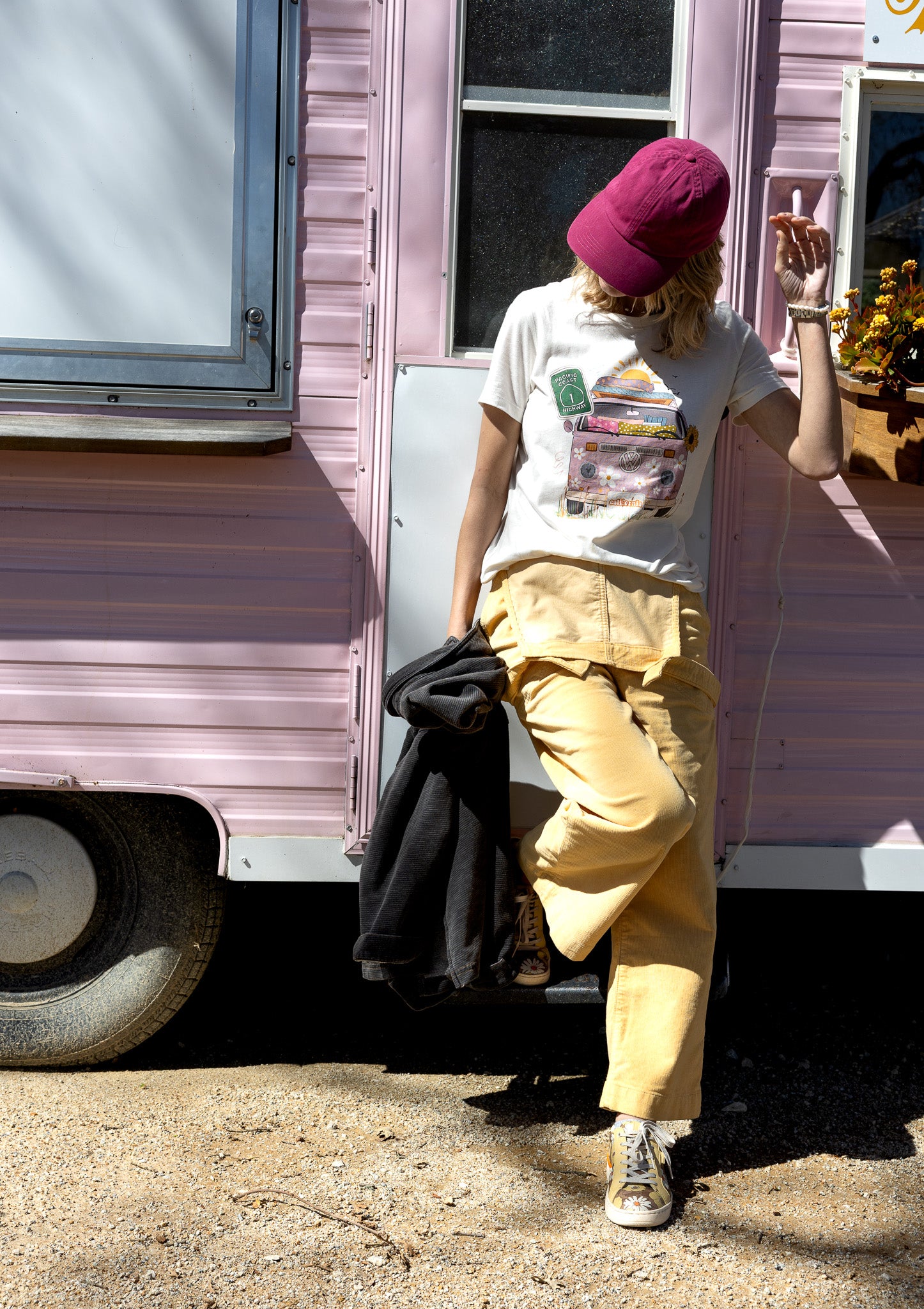 Hand-illustrated graphic tee featuring a vibrant pink and floral Hippie bus with California license plate and Highway 1 sign.