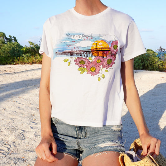 This surfer girl's dream destination tee features a stunning hand-illustrated design of the iconic Newport Beach Pier, surrounded by beautiful floral details.&nbsp;  Soft, comfortable, and perfect for beachy vibes or everyday wear, this tee is a must-have for any surfer girl or beach lover.