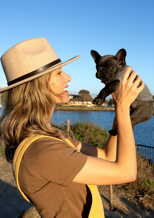Artist Nadia Watts holding her French Bulldog puppy while wearing a North Shore Girls t-shirt.