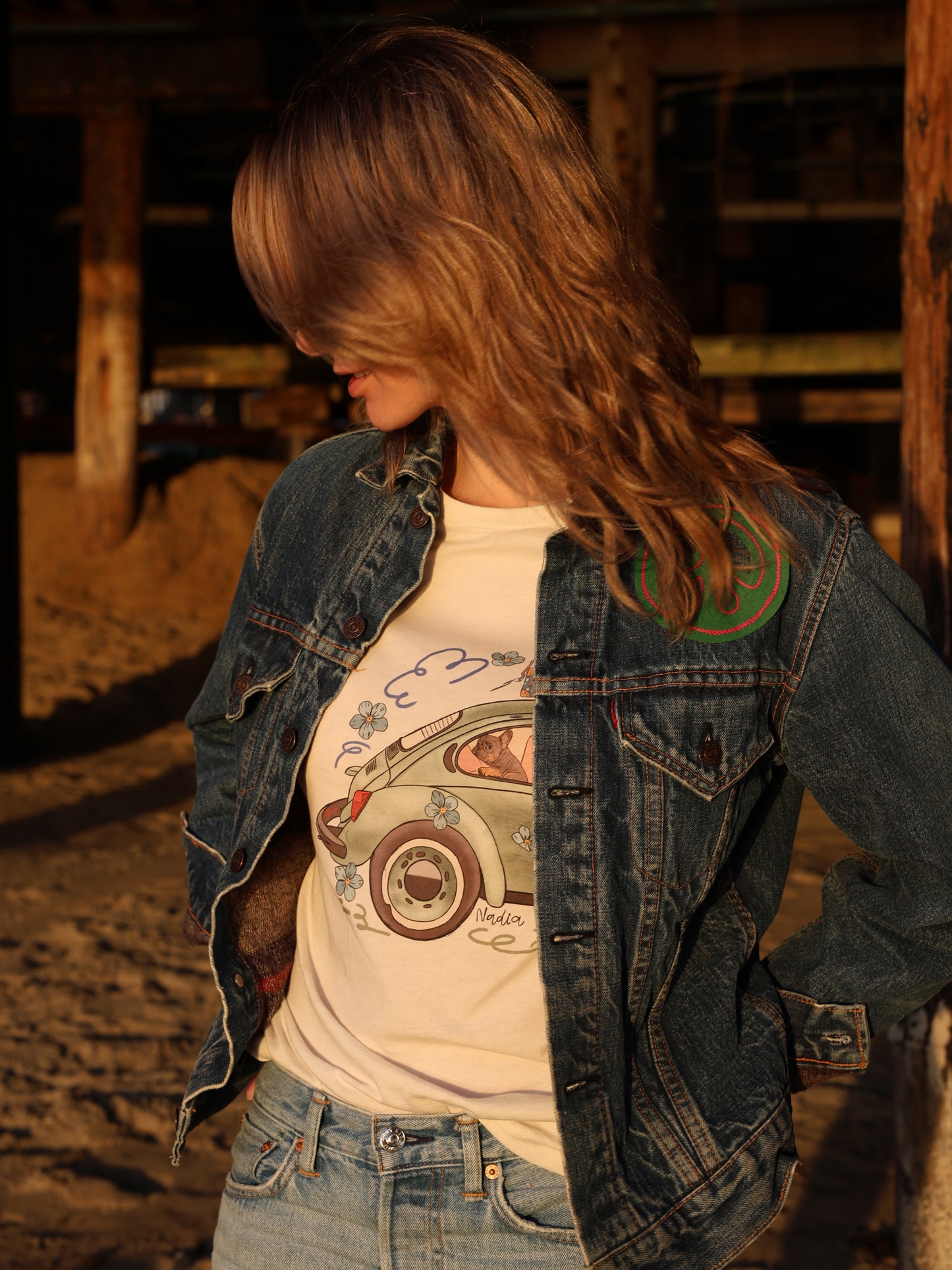 Woman wearing a cream-colored North Shore Girls tee with an illustration of a green vintage car and a French Bulldog