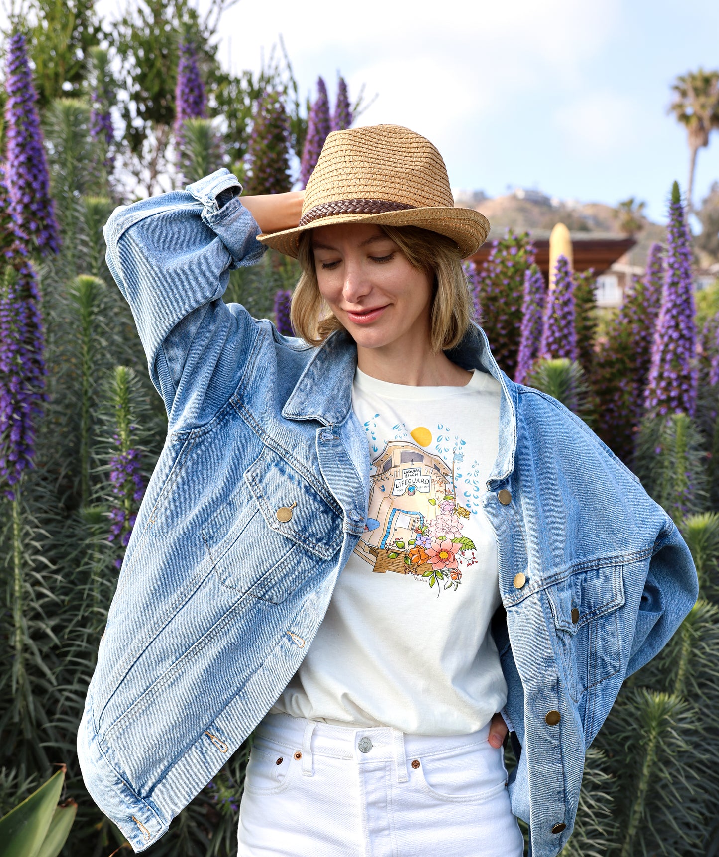 Nadia Watts -artist and graphic designer wearing her graphic tee featuring  an illustration of Laguna Beach Lifeguard Tower