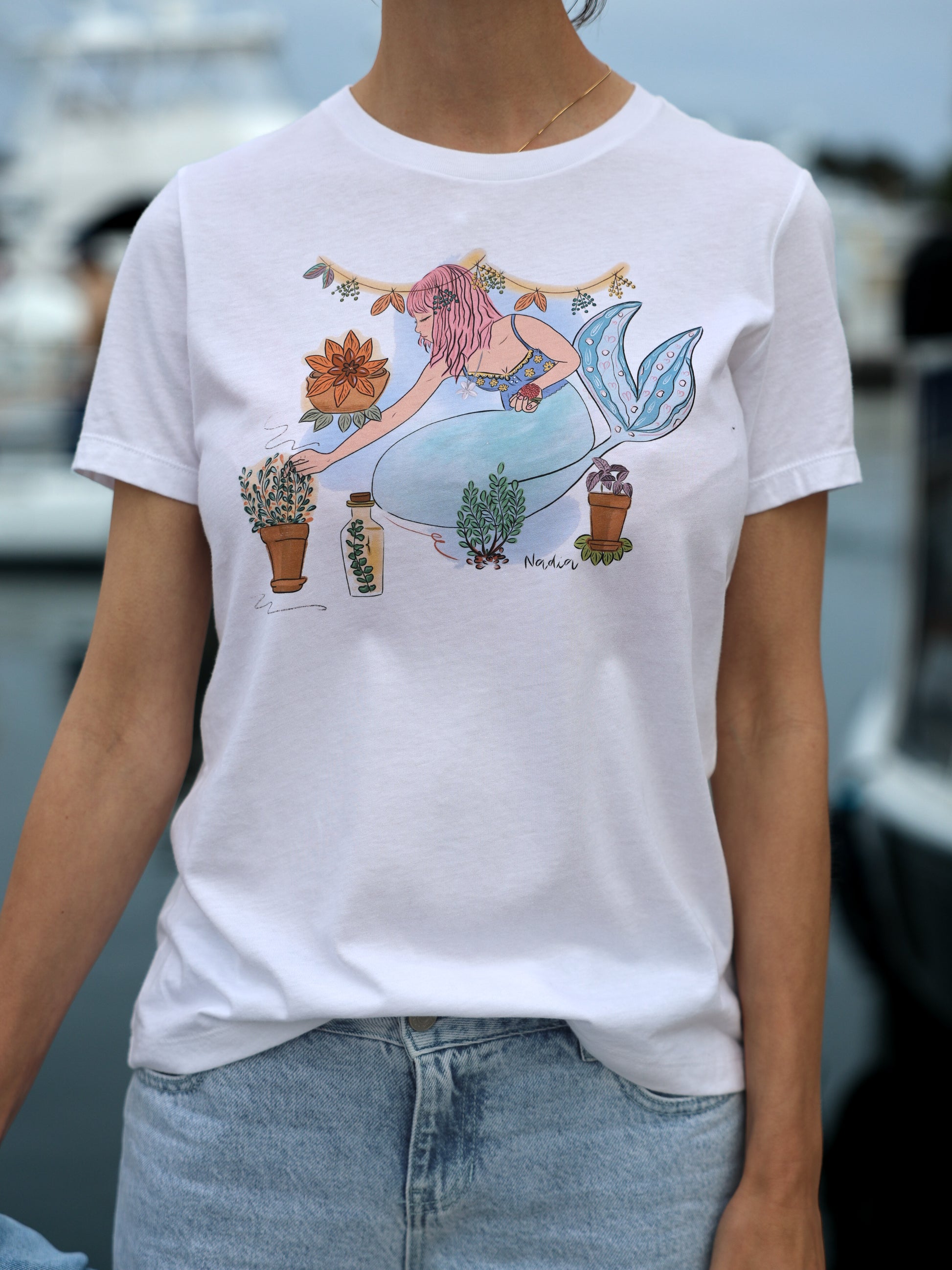 Mermaid tee featuring a hand-illustrated design of a pink-haired mermaid surrounded by herbs and seaweed, symbolizing growth and harmony between ocean and earth