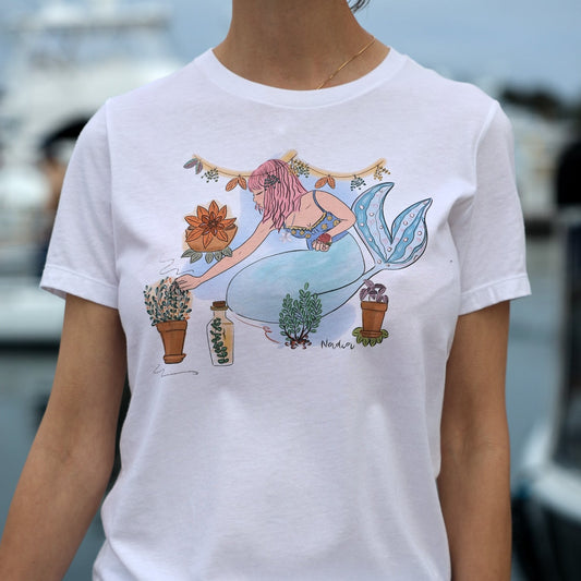 Mermaid tee featuring a hand-illustrated design of a pink-haired mermaid surrounded by herbs and seaweed, symbolizing growth and harmony between ocean and earth