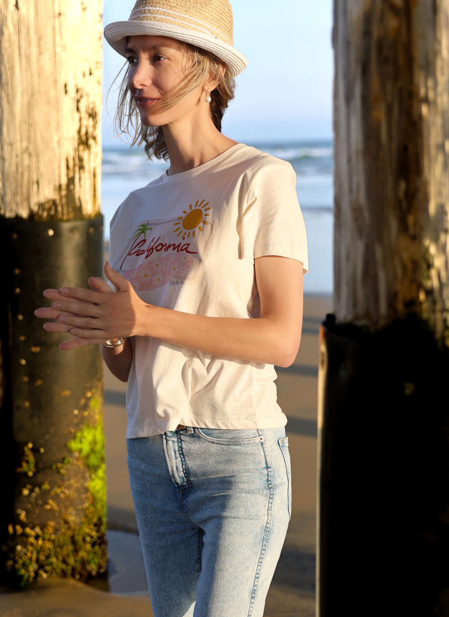 Relaxed fit women's graphic tee with hand-drawn California design, featuring a pink floral surfboard, palm tree, and sun on a white background