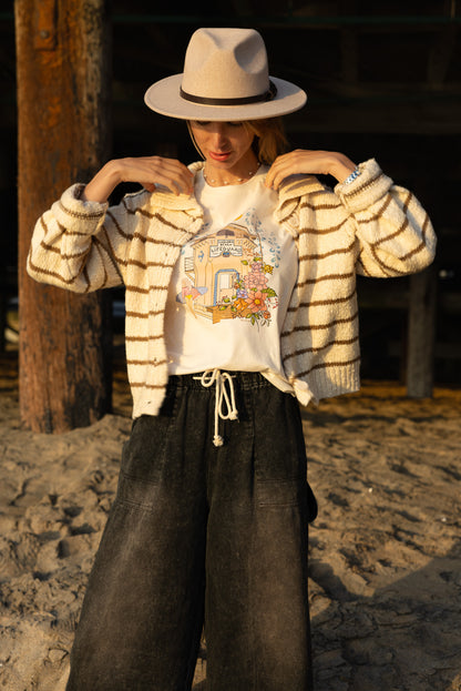 Woman wearing a cream North Shore Girls tee with an illustration of the Laguna Beach lifeguard tower and a surfer.
