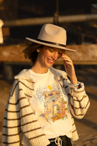 Woman wearing a cream North Shore Girls tee with an illustration of the Laguna Beach lifeguard tower and a surfer.