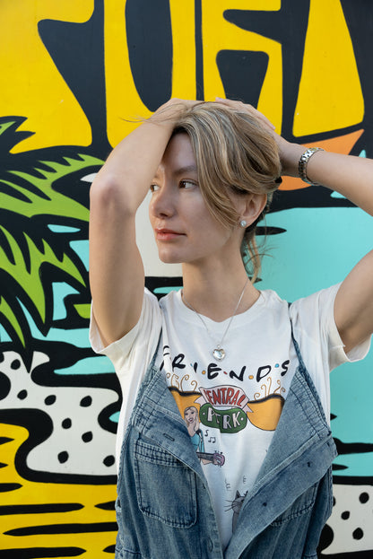 Woman wearing a white North Shore Girls tee with a hand-drawn illustration of a woman playing guitar and a "Smelly Cat"