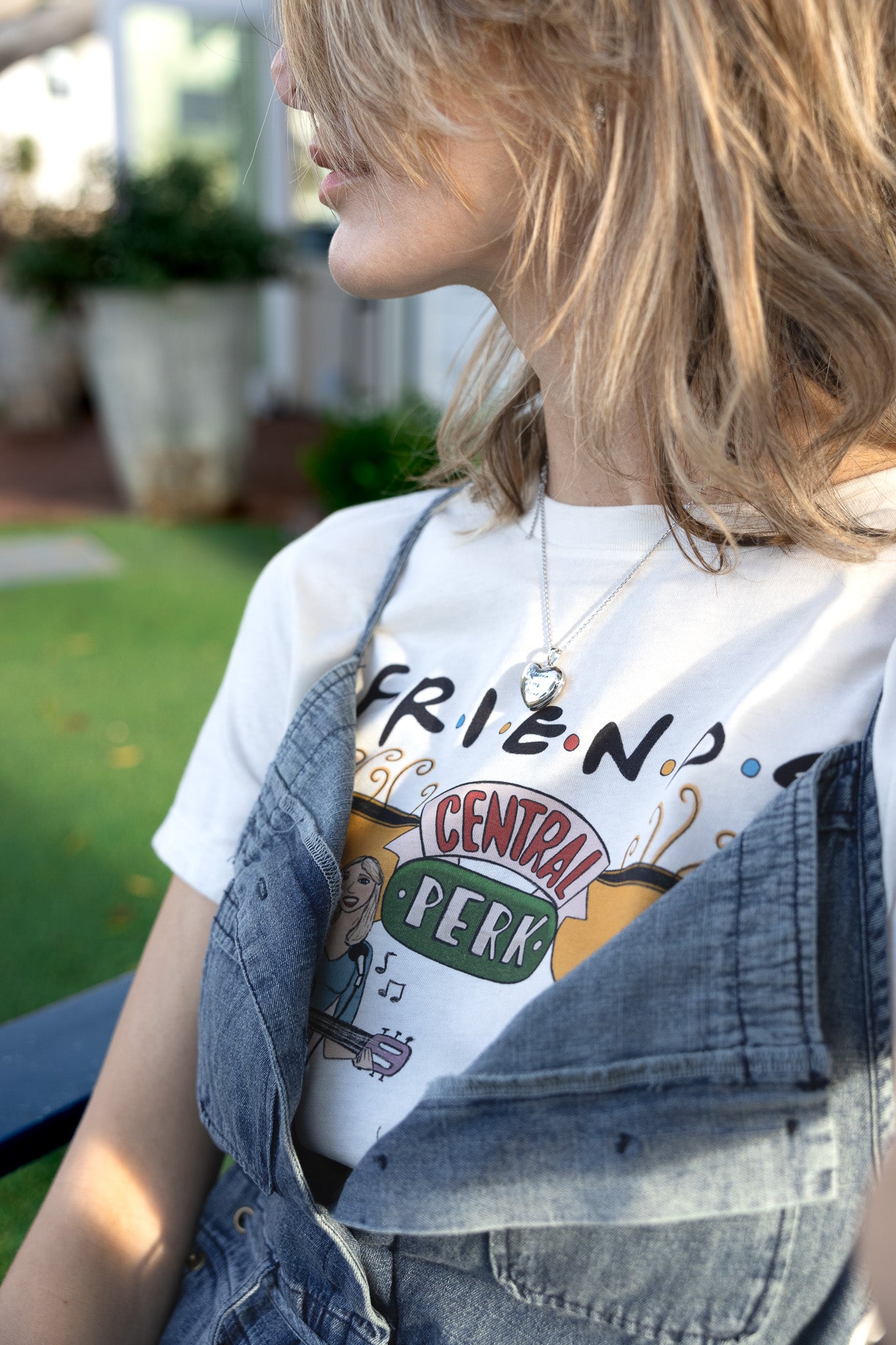 Woman wearing a white North Shore Girls tee with a hand-drawn illustration of a woman playing guitar and a "Smelly Cat"