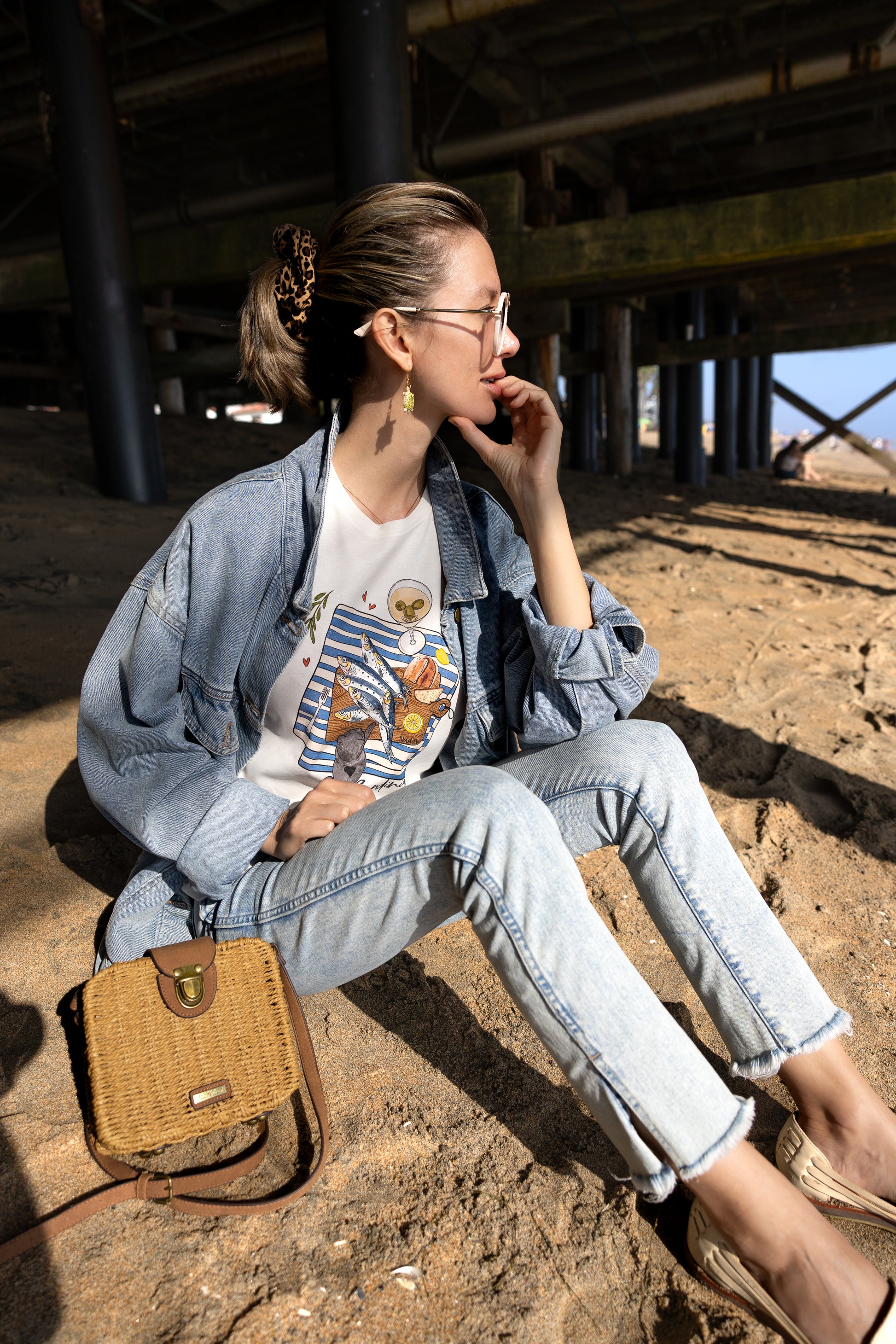 Woman is wearing a graphic tee with hand-illustrated sardines on a cutting board, dirty martini, bread, lemon, and a cute cat reaching for sardines. SARDINIA slogan