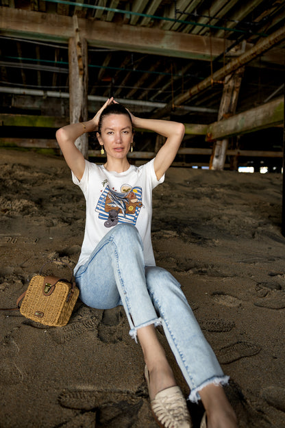 Sardinia illustrated tee showing hand‑drawn sardines, a dirty martini, bread, lemon, and a cat on an off‑white cotton shirt