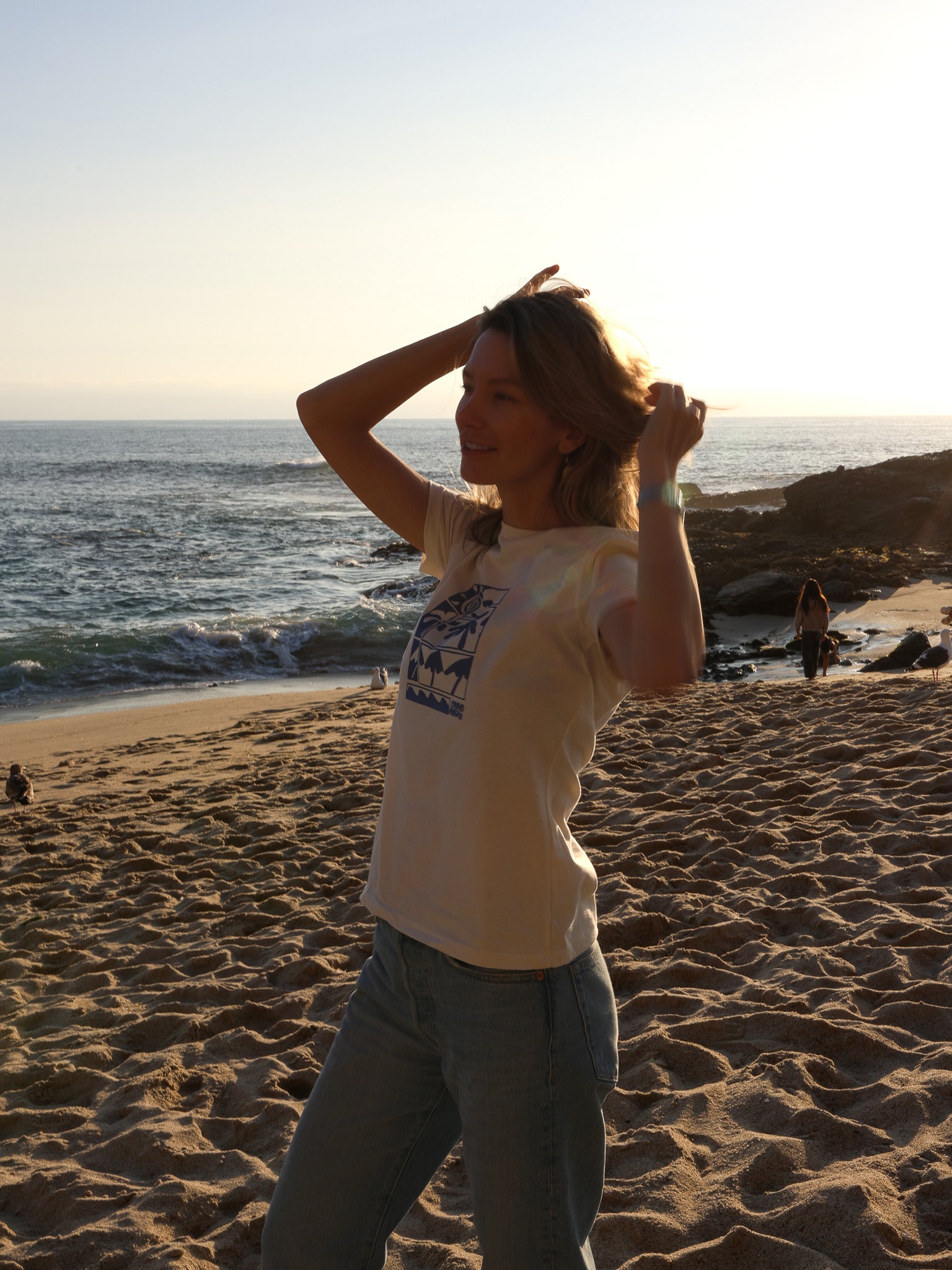 Women's cream-colored tee with a blue stylized illustration of palms and ocean waves.