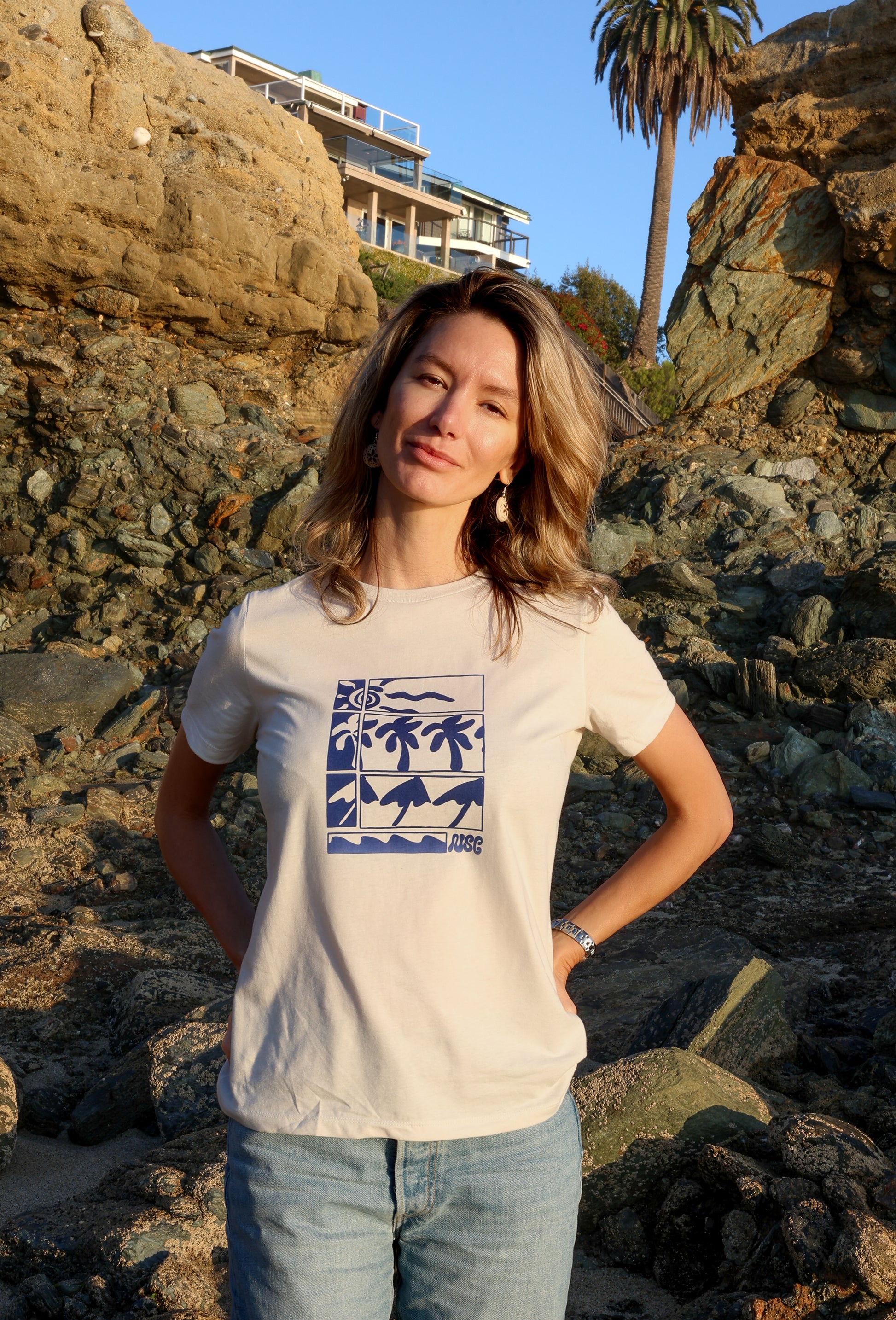 Woman wearing a white t-shirt with a graphic design, standing on a rocky beach.