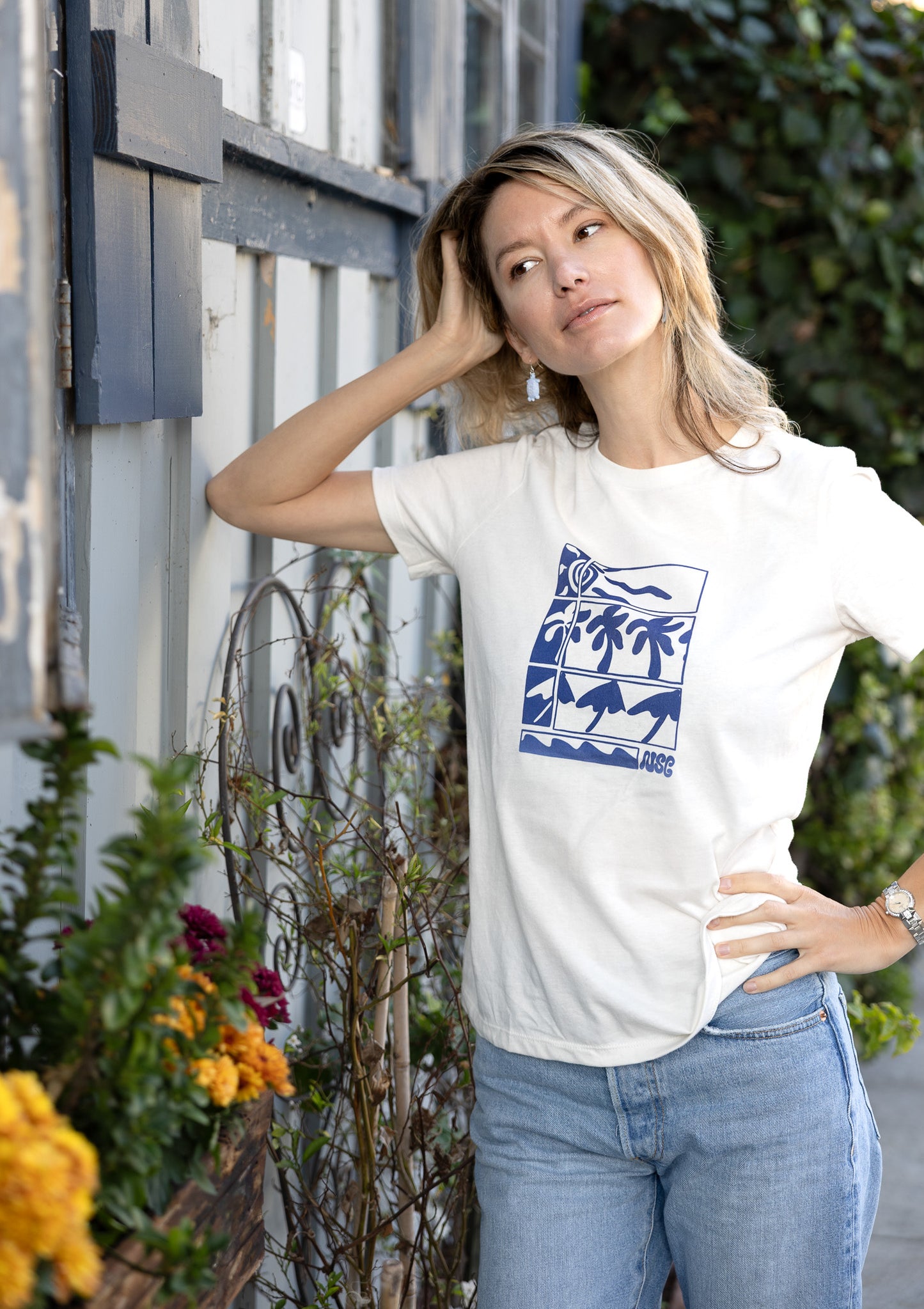 Women's cream-colored tee with a blue stylized illustration of palms and ocean waves.