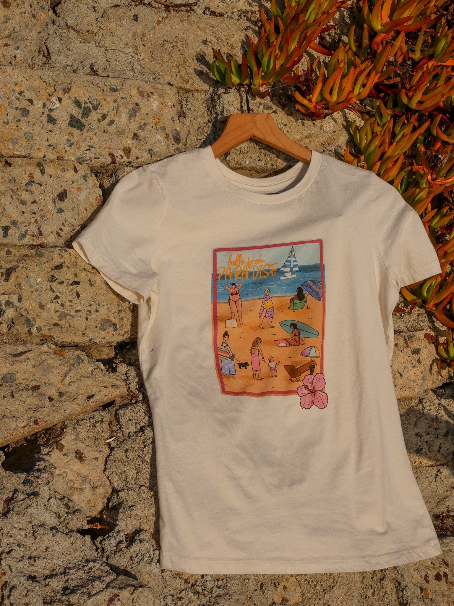 Women's soft cotton t-shirt with a hand-drawn "Hello from Paradise" tropical beach scene, North Shore Girls brand.