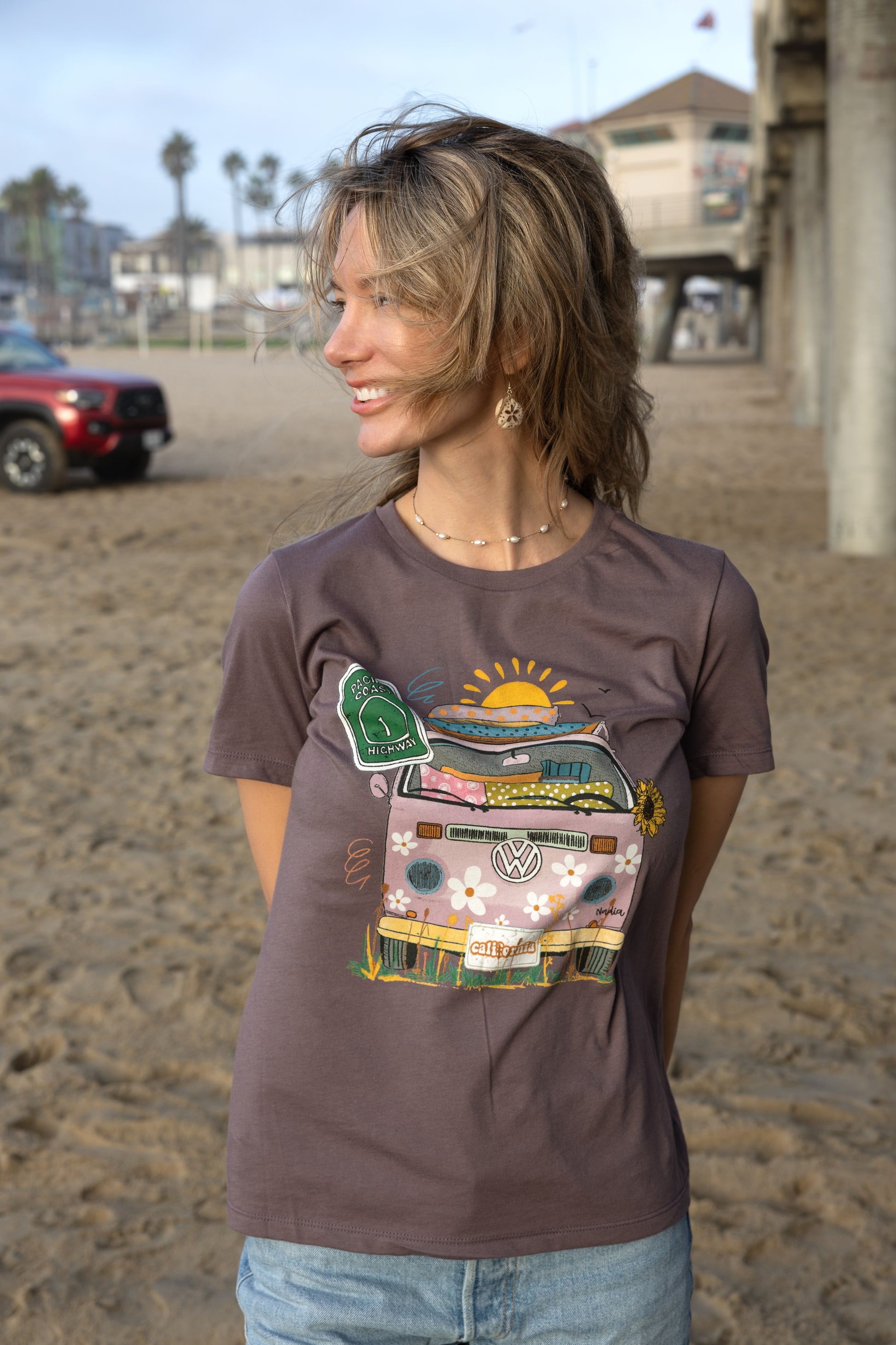 Woman in a purple North Shore Girls graphic t-shirt features a hand-drawn vintage floral beach van.