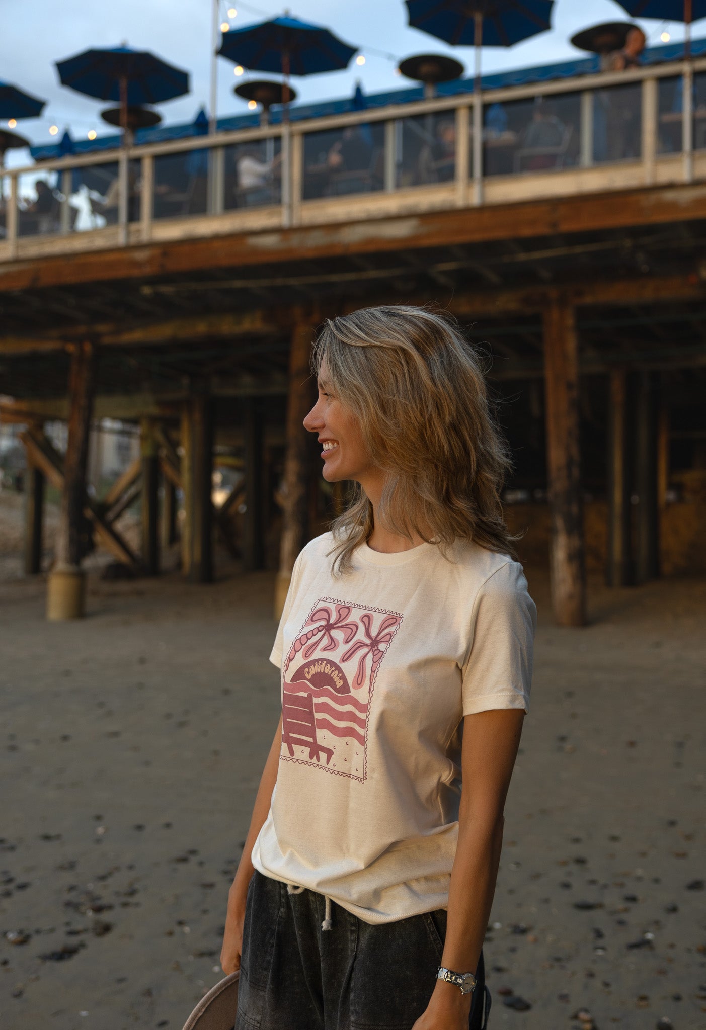 Women's cream-colored tee with a mauve postage stamp illustration of a beach chair and palms.