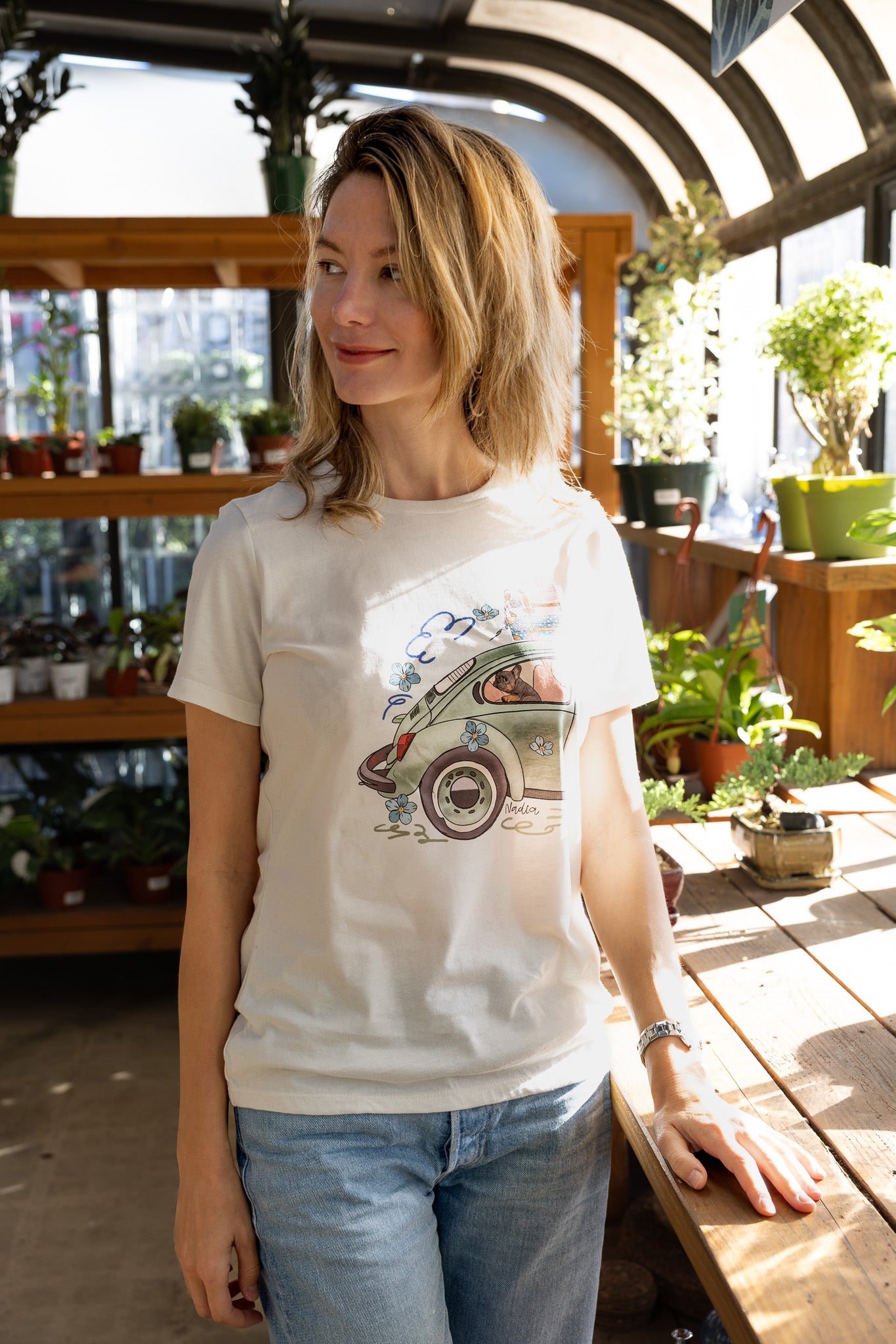 Woman wearing a cream-colored North Shore Girls tee with an illustration of a green vintage car and a French Bulldog