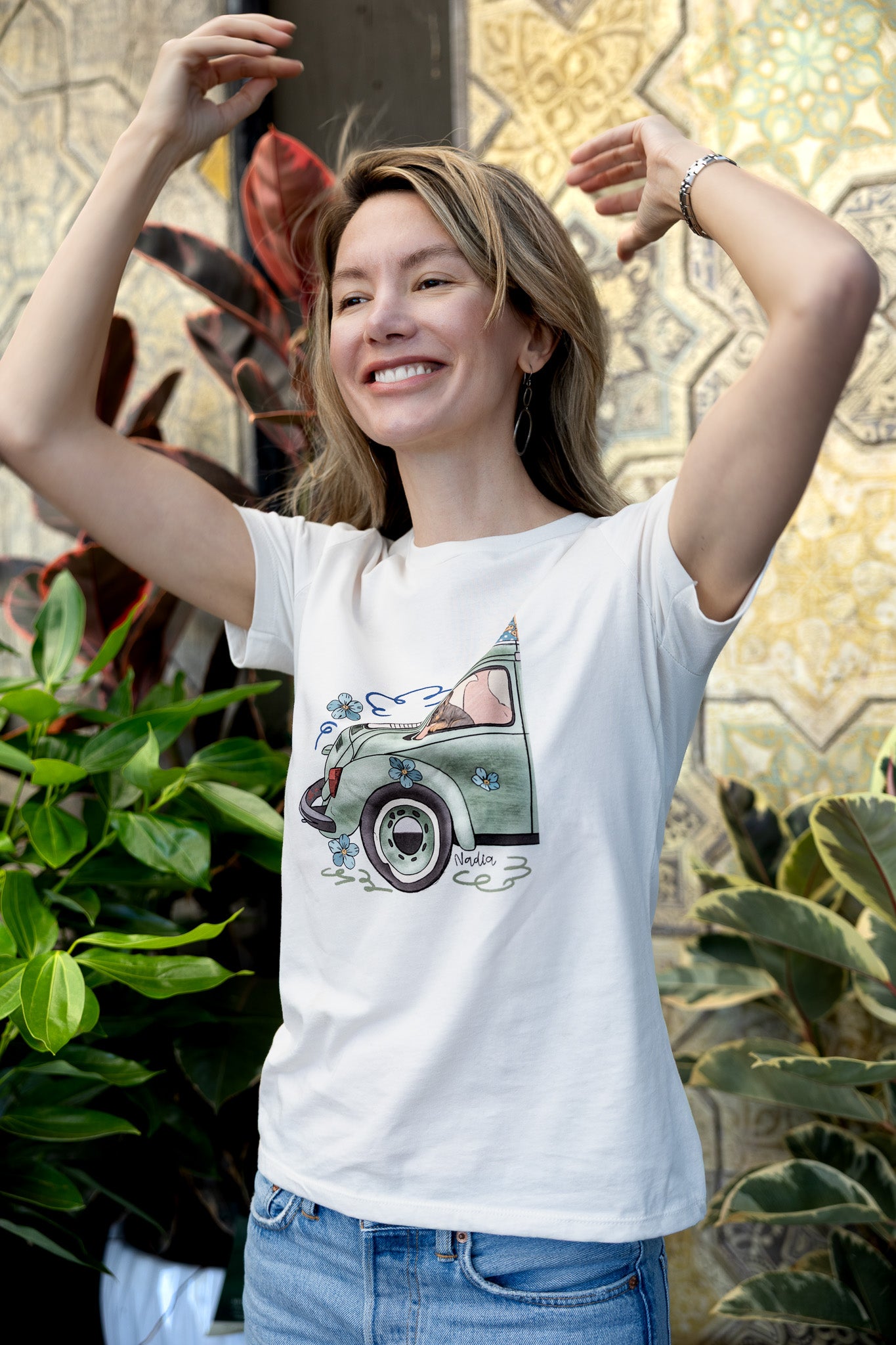 Woman wearing a cream-colored North Shore Girls tee with an illustration of a green vintage car and a French Bulldog