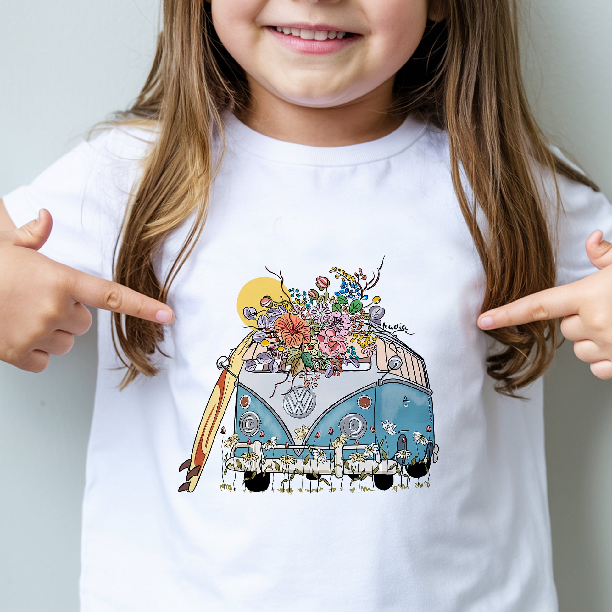 Child wearing a white t-shirt with a colorful graphic of a van and flowers, pointing at the design.