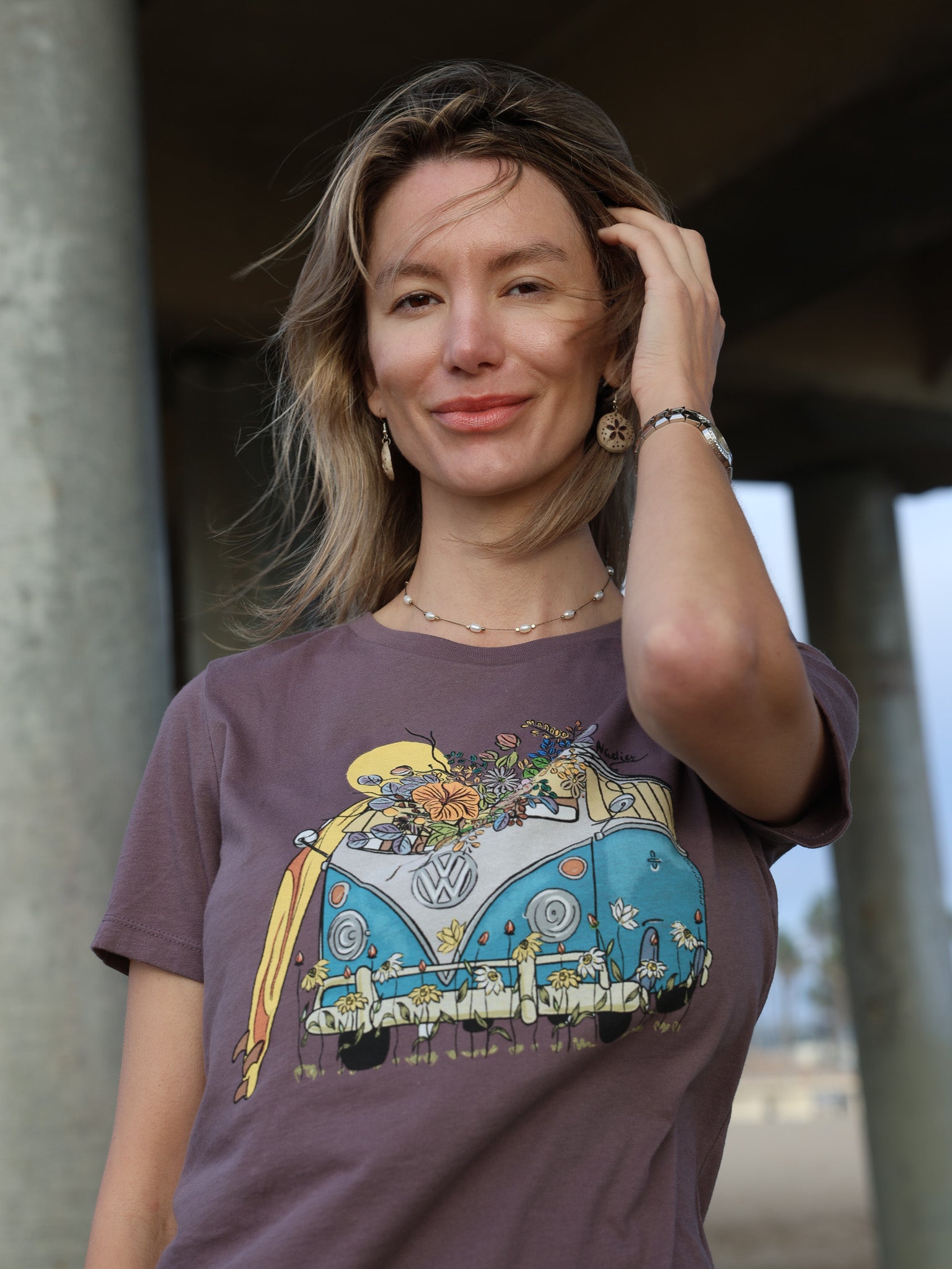 Woman wearing a North Shore Girls tee with an illustration of a blue van, surfboard, and flowers.
