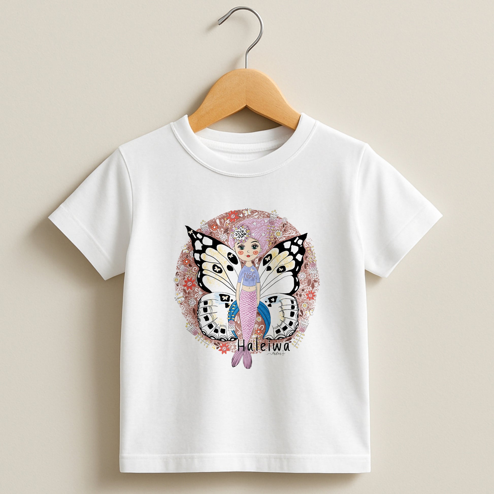 White toddler t-shirt featuring a hand-drawn mermaid with butterfly wings and floral patterns, labeled Haleiwa.