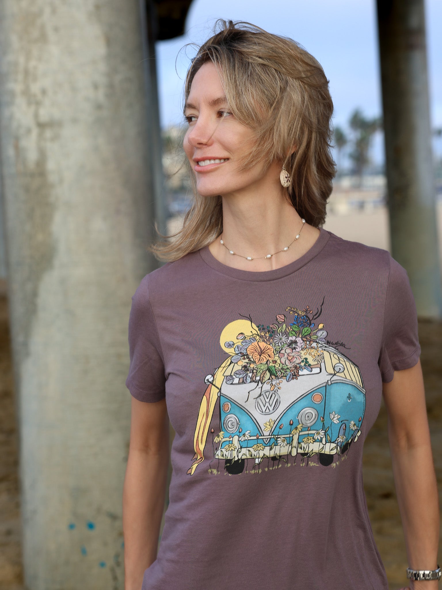 Woman wearing a North Shore Girls tee with an illustration of a blue van, surfboard, and flowers.