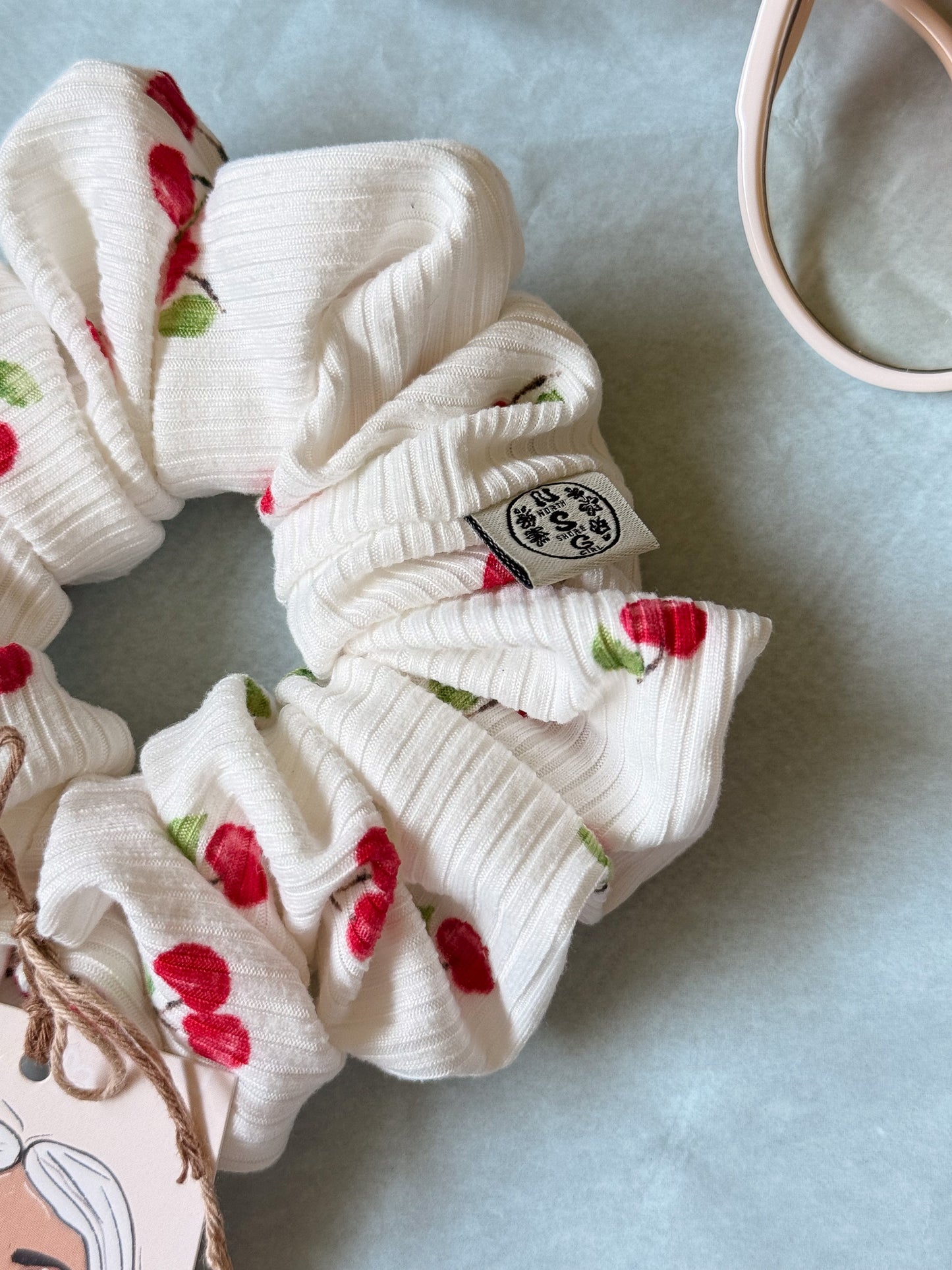 White scrunchie with red floral patterns on a light blue background