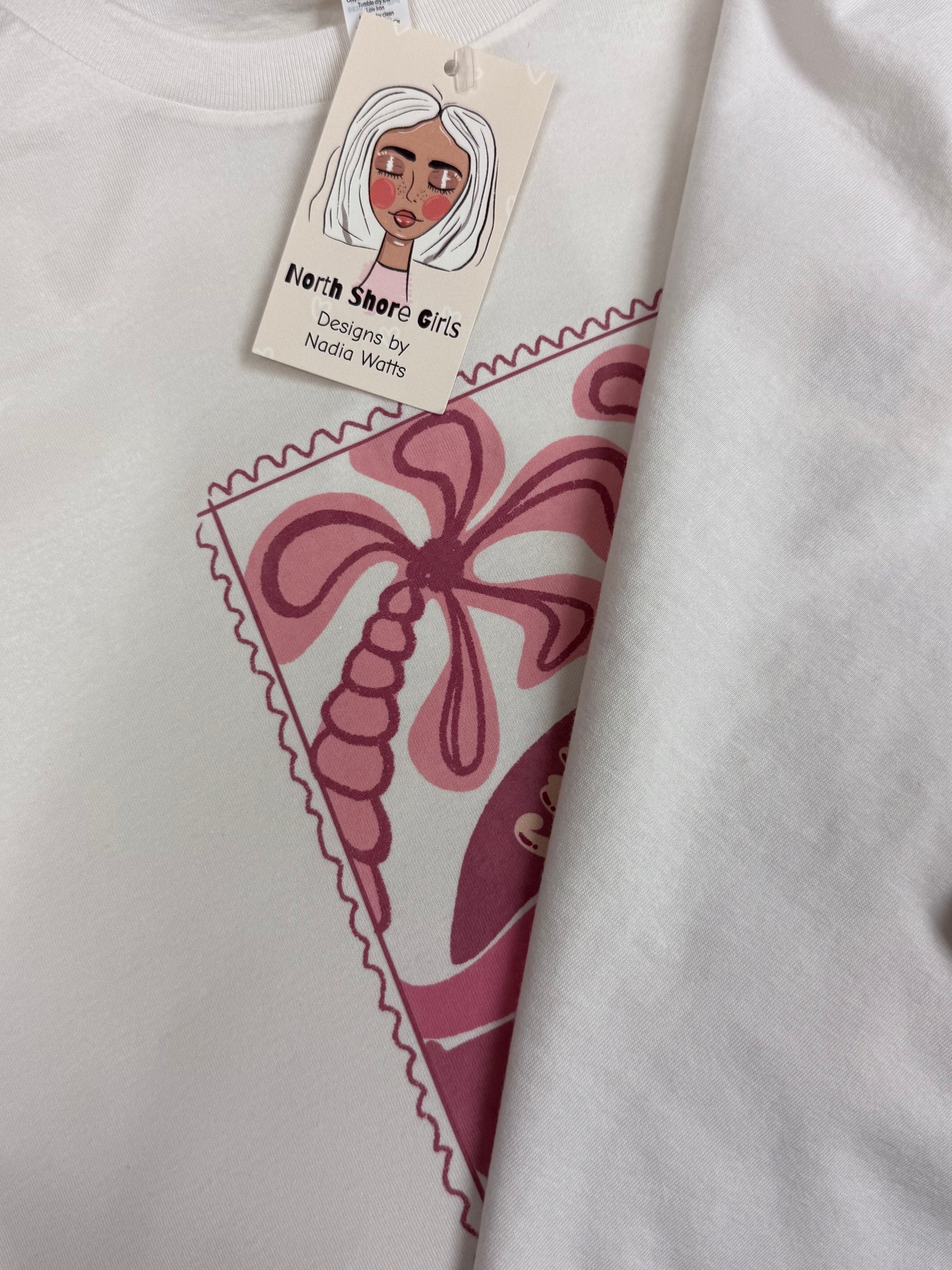 White t-shirt with pink graphic design and a tag featuring a stylized face.