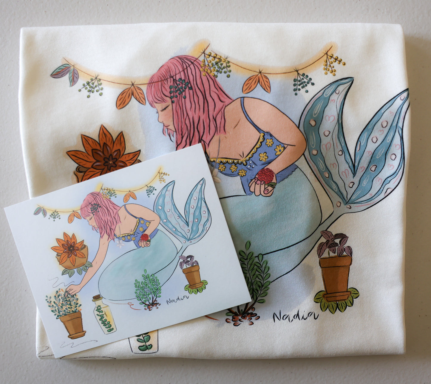 Youth white t-shirt with a hand-drawn mermaid tending to bohemian potted garden plants, North Shore Girls brand.