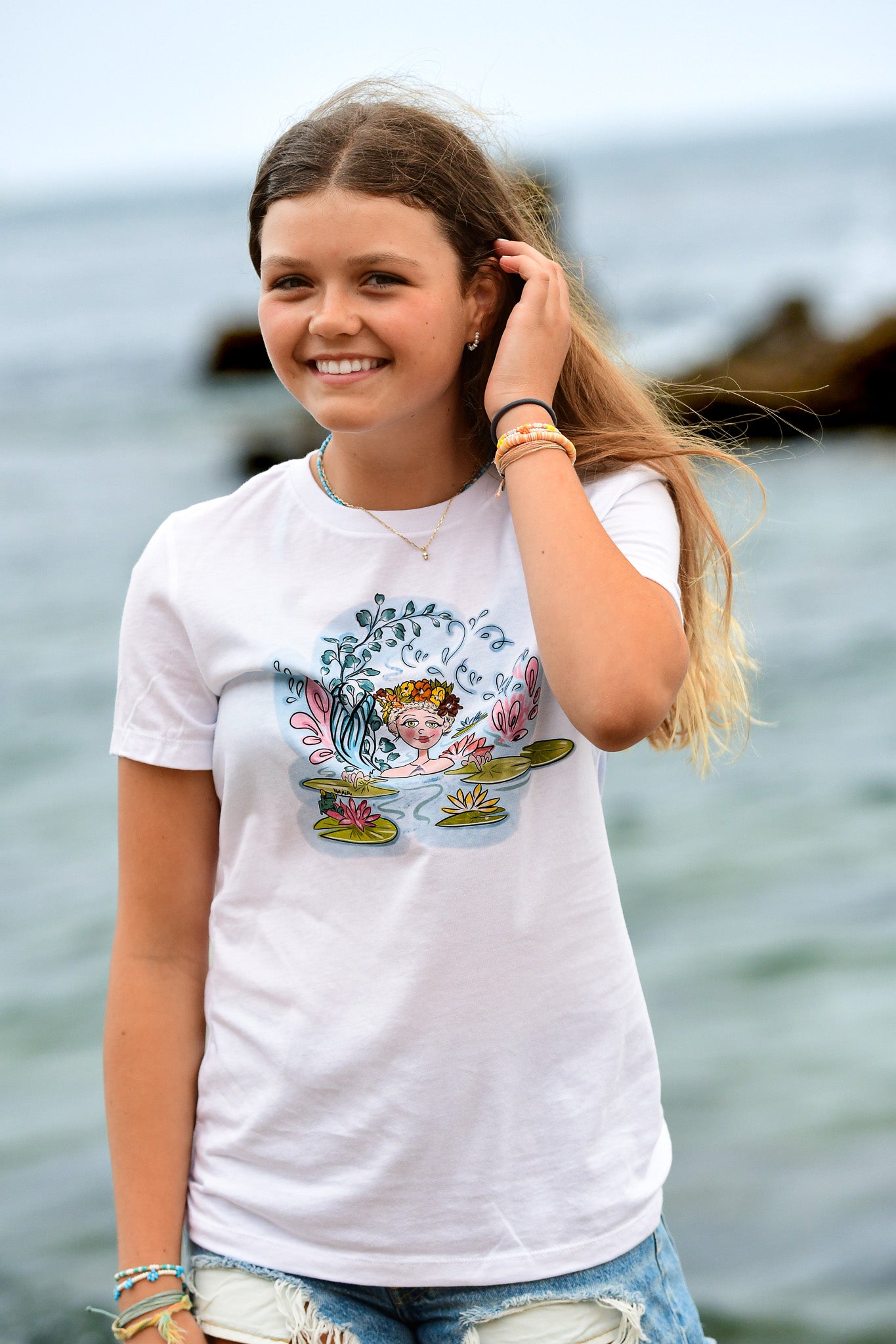Youth white t-shirt featuring a hand-drawn mermaid with a floral wreath and tail among water lilies, North Shore Girls brand.