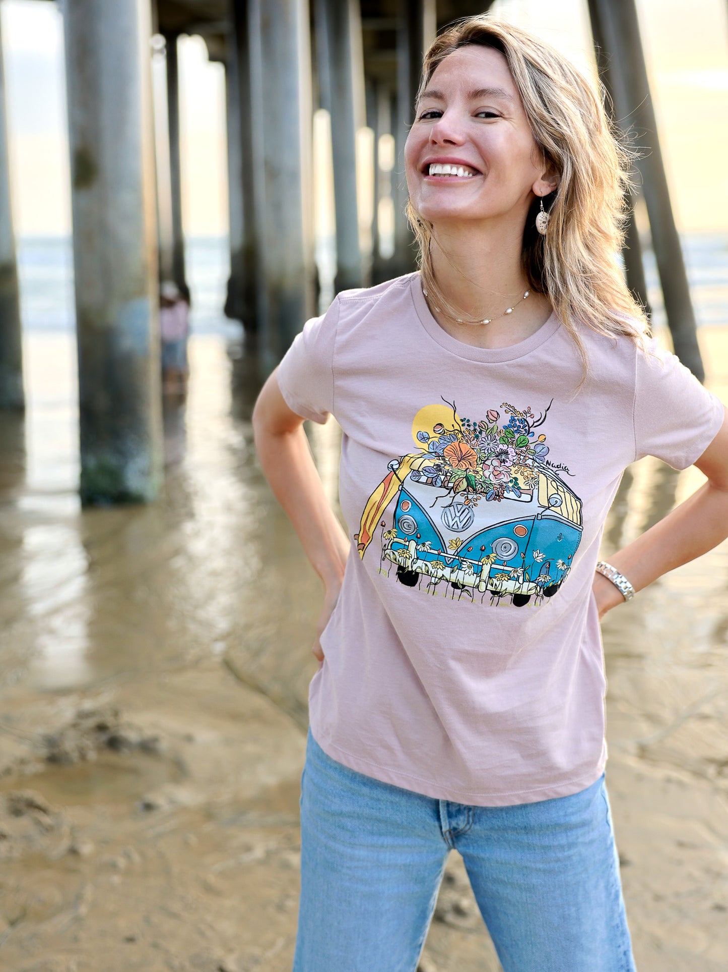 Woman wearing a North Shore Girls tee with an illustration of a blue van, surfboard, and flowers.