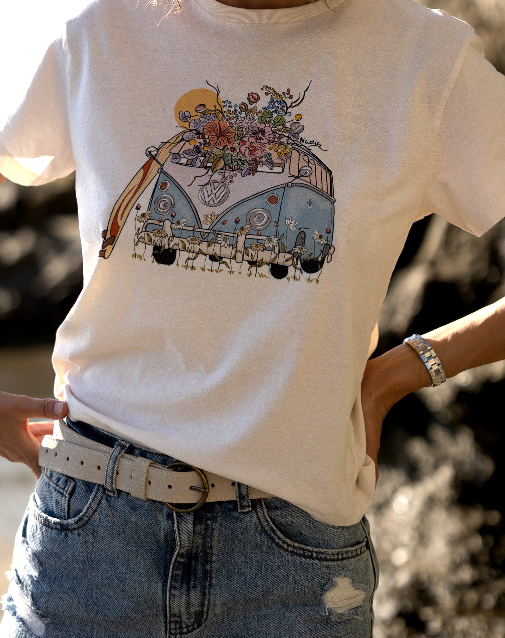 Hand-illustrated graphic tee featuring a colorful surf bus surrounded by floral details. The tee is a relaxed fit, made from 100% cotton, and includes the artist's signature.