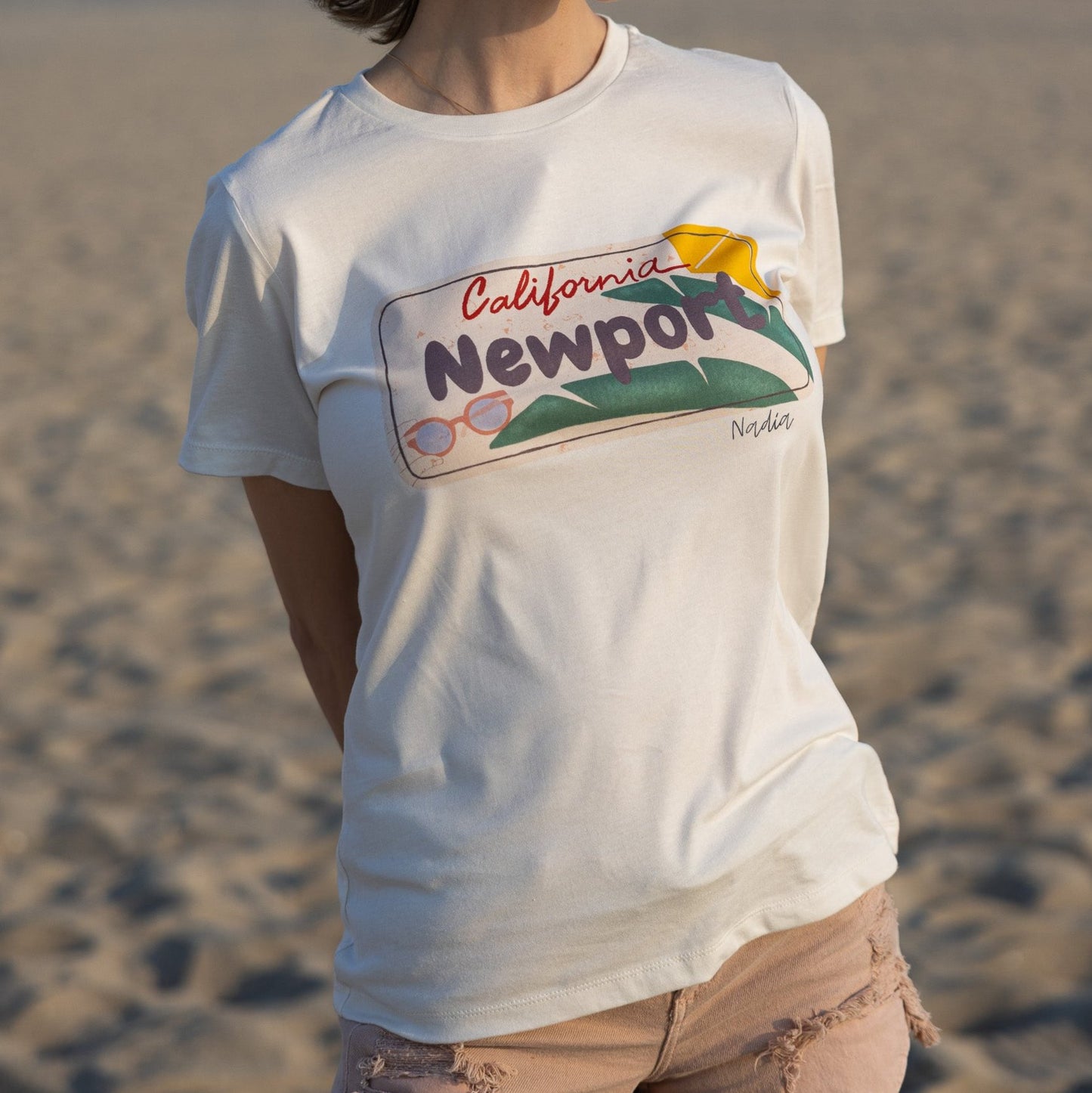 Woman is wearing North Shore Girls tee with a Newport California license plate illustration and palm leaves.