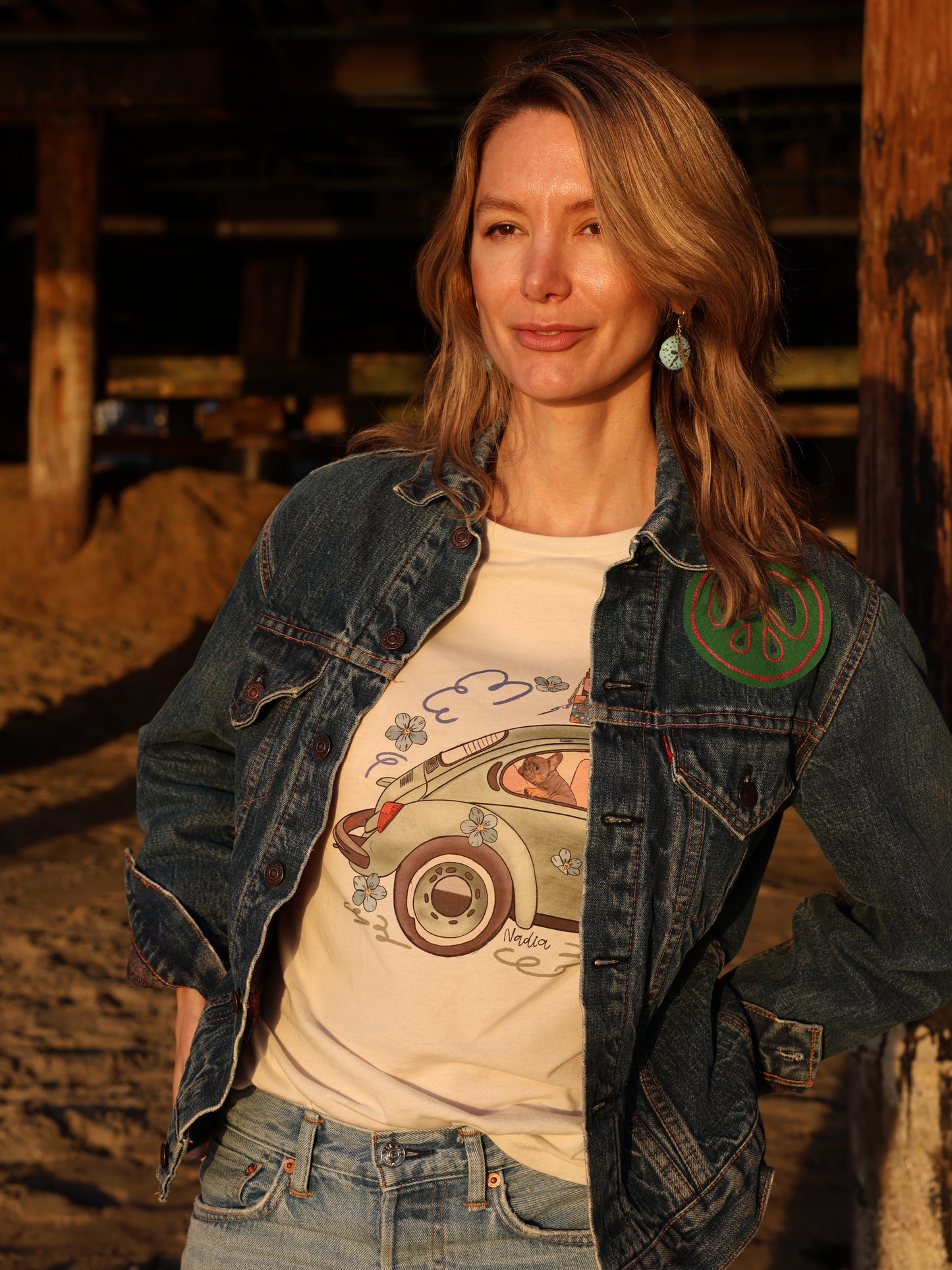 Woman wearing a cream-colored North Shore Girls tee with an illustration of a green vintage car and a French Bulldog