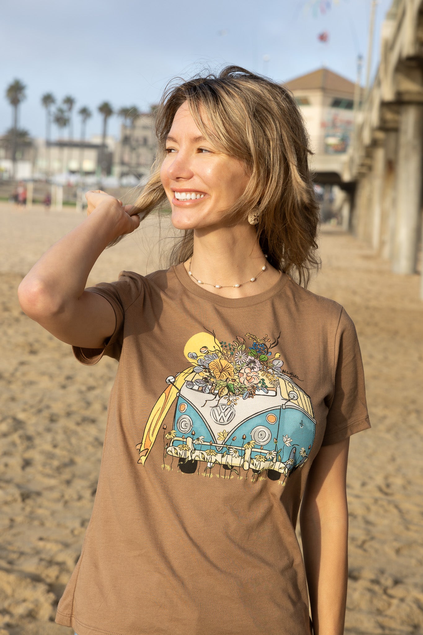 Woman wearing a brown t-shirt with a colorful graphic design on a beach.