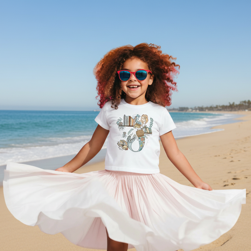  a girl is modeling and Illustrated toddler tee with a graphic of a mermaid standing next to a bookshelf