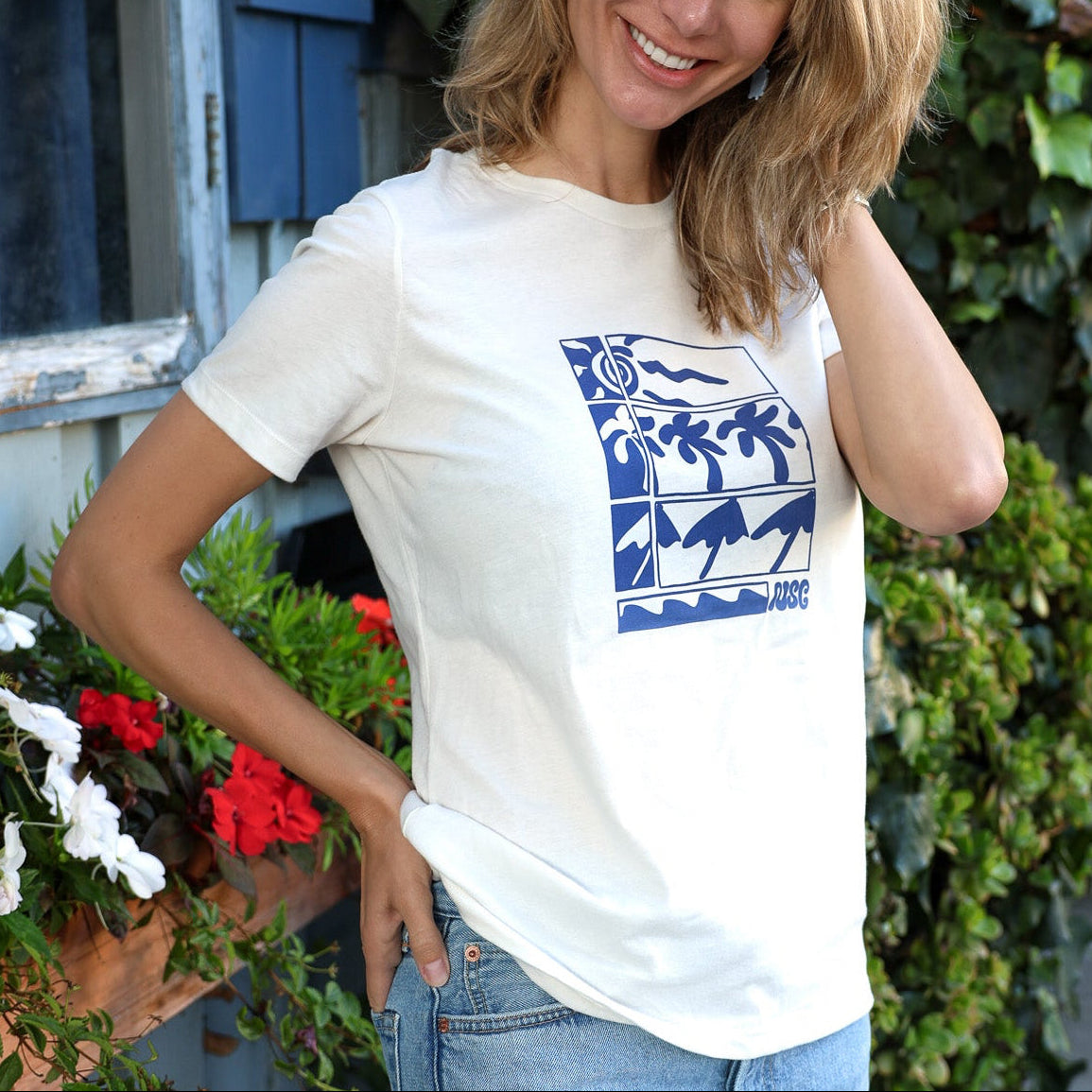 Women's cream-colored tee with a blue stylized illustration of palms and ocean waves.