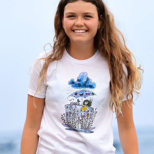 Whimsical handmade graphic tee by North Shore Girls. A cute girl holding umbrella, her cat is sleeping next to her. They are hiding in a floral tea cup from the rain. Cute and fun beach tee for girls. Designed and printed by an artist. 