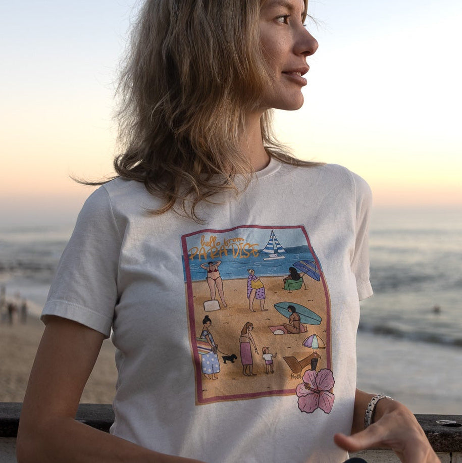 Women's soft cotton t-shirt with a hand-drawn "Hello from Paradise" tropical beach scene, North Shore Girls brand.