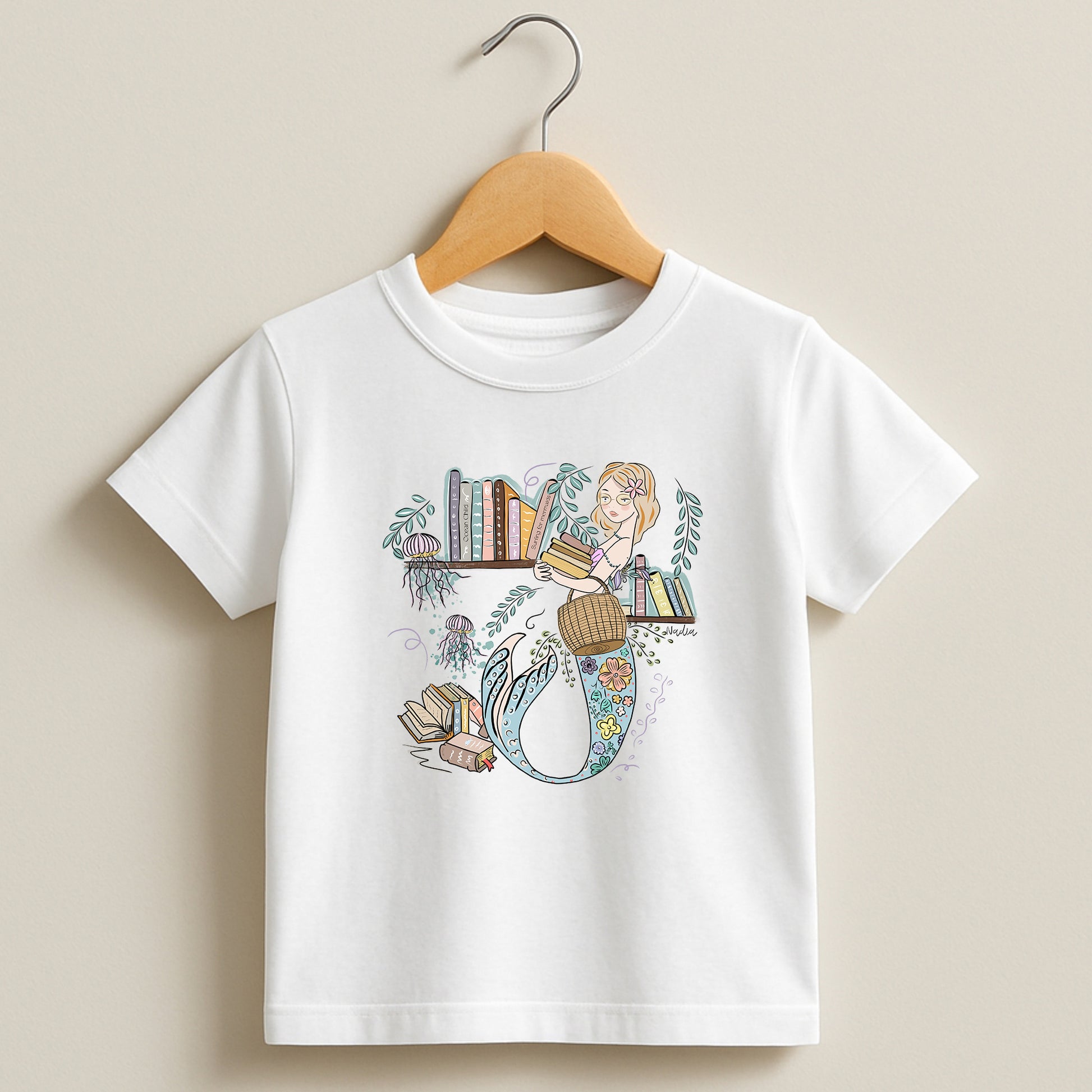 Illustrated toddler tee showing a mermaid with glasses next to a bookshelf, holding books – literary ocean theme