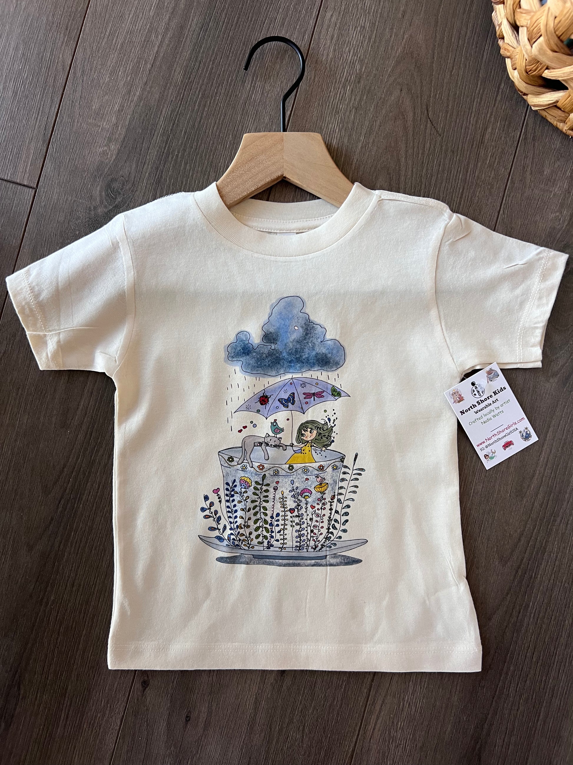 toddler t-shirt with a hand-drawn illustration of a girl and cat in a teacup garden under a rain cloud, part of the North Shore Kids collection