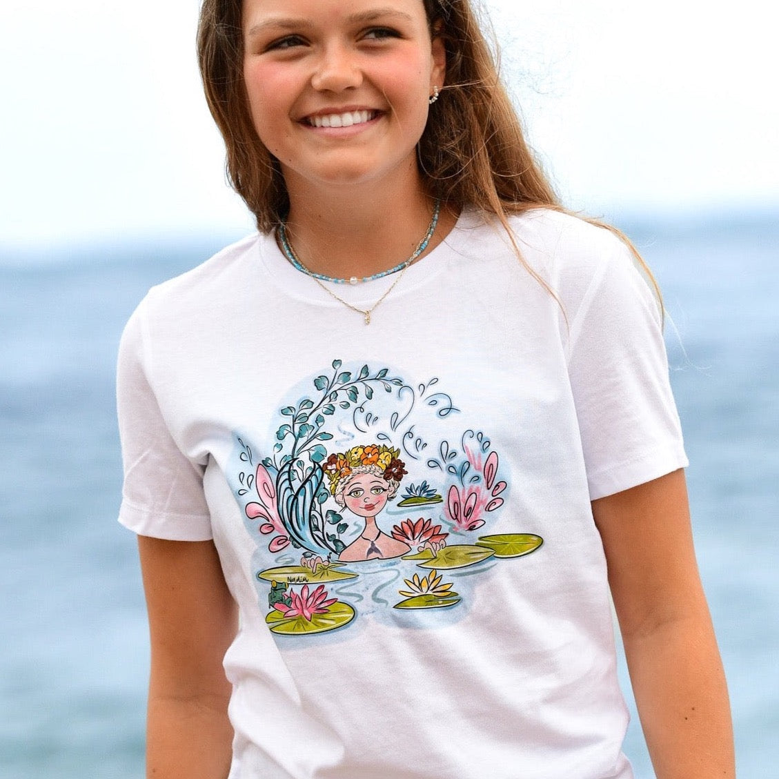Youth white t-shirt featuring a hand-drawn mermaid with a floral wreath and tail among water lilies, North Shore Girls brand.
