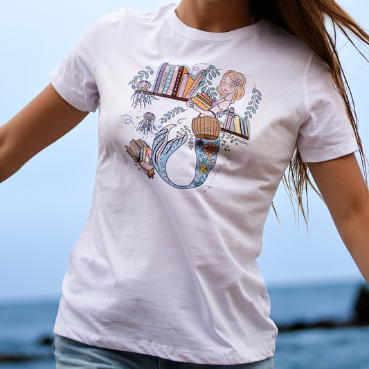 Illustrated graphic tee featuring a mermaid librarian surrounded by books and ocean elements, with a whimsical and colorful design that combines a love of reading and mythical creatures, printed on a soft and relaxed-fit cotton t-shirt.