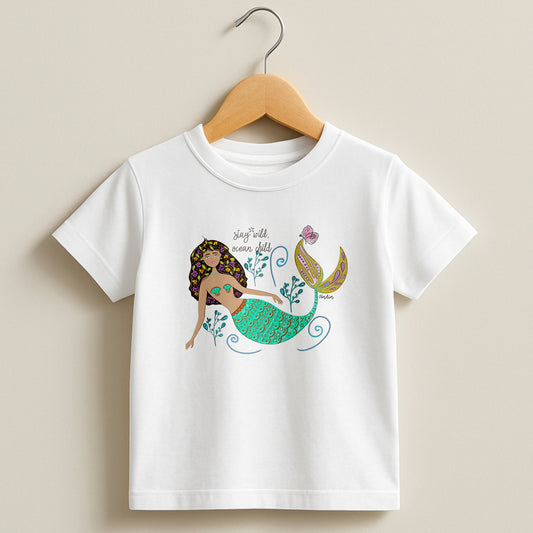 White toddler t-shirt featuring a hand-drawn mermaid with flowers in her hair and "Stay Wild Ocean Child" text, signed by the artist