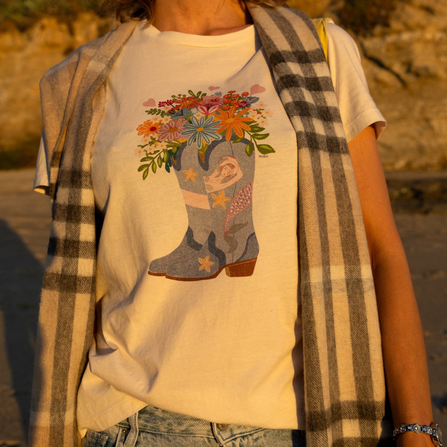 Women's white graphic t-shirt featuring a hand-drawn cowboy boot with a mermaid and flowers, North Shore Girls brand.